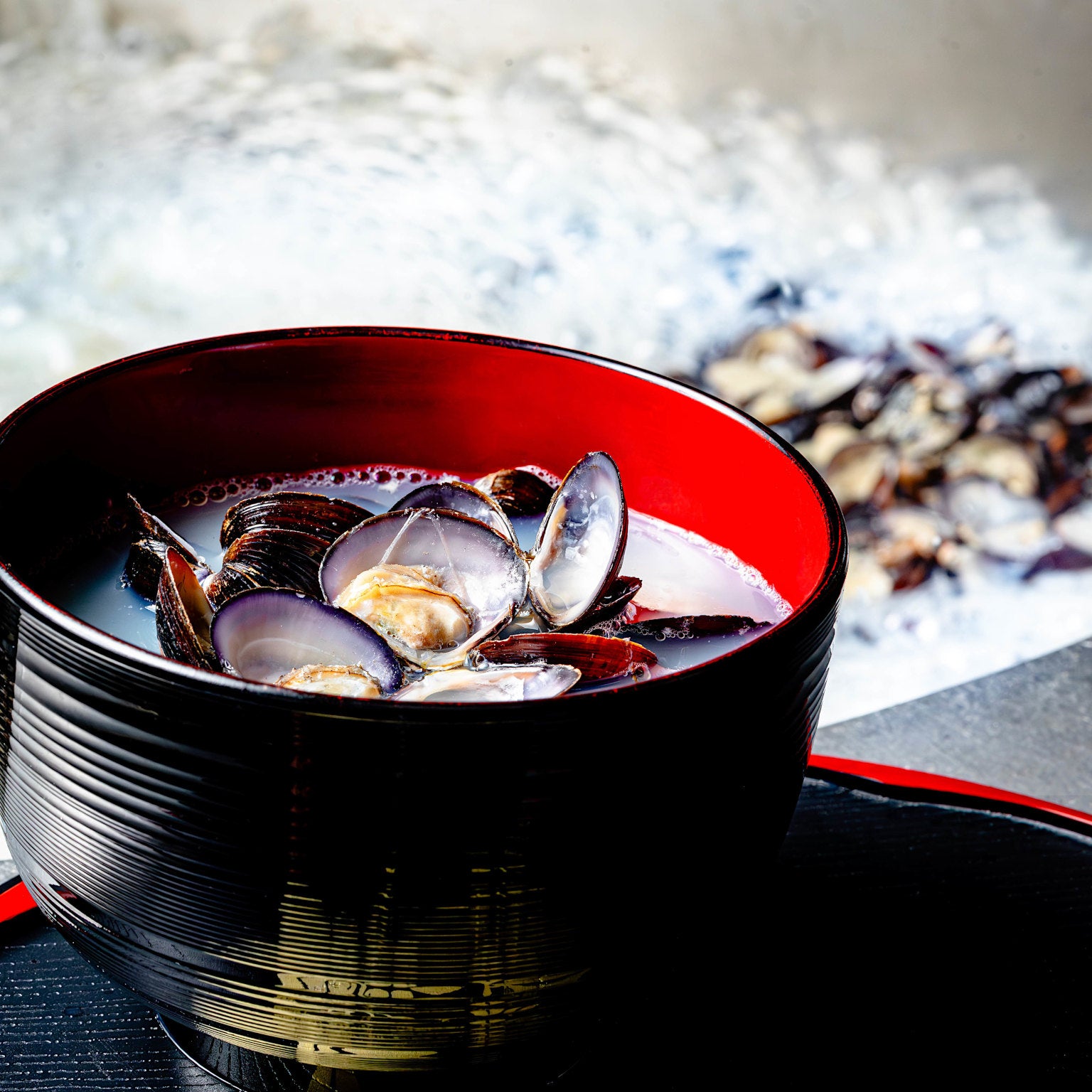 シジミエキス肝助の製造風景で、大釜でしじみ貝を煮出しているシーンです。手前にお椀に入ったしじみ貝とその潮汁が置かれています。